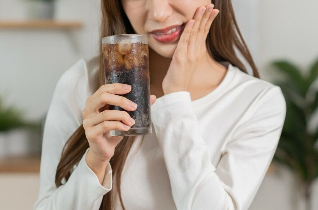 Gesundheit asiatische junge Frau, Mädchen Hand berührt ihren Mund, leiden unter Zahnschmerzen, Karies oder Empfindlichkeit Kavität Backenzahn oder Entzündung trinken kalt, sprudelndes Wasser zu Hause. Empfindliche Zähne Konzept.