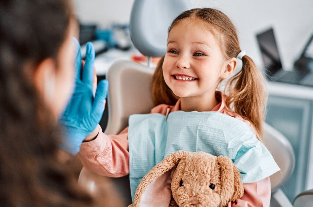 Beim Arztbesuch. Ein ehrliches, emotionales Foto von einem Kind, das auf einem Zahnarztstuhl sitzt, ein Spielzeugkaninchen in der Hand hält und der Krankenschwester fröhlich die Daumen drückt.