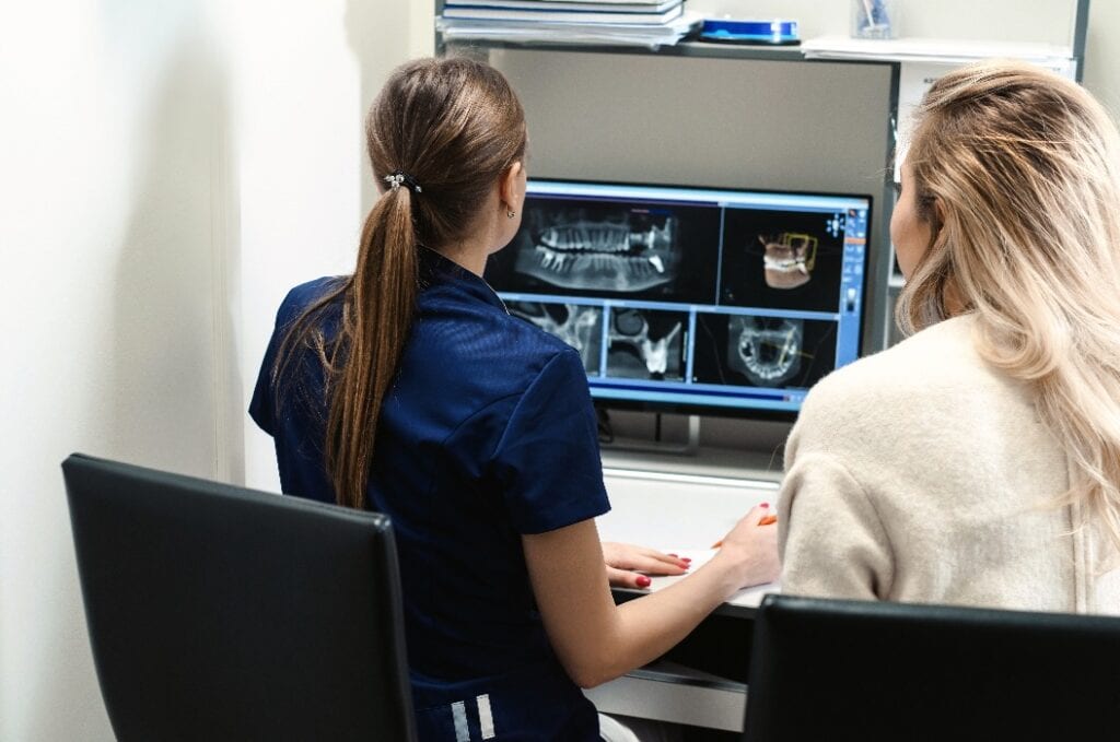 Eine Ärztin zeigt dem Patienten ein Röntgenbild am Bildschirm. Computerdiagnose Zahntomographie. Planung einer Zahnbehandlung in einer modernen Zahnklinik