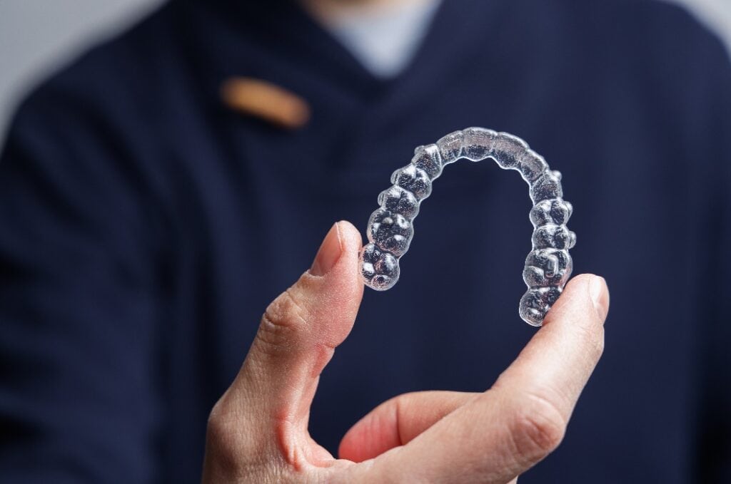 Mann hält einen transparenten Aligner. Invisalign Kieferorthopädie con