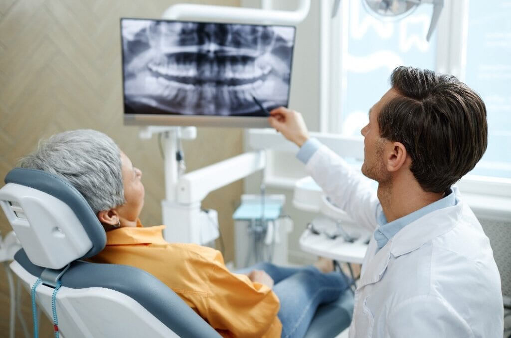 Rückansicht eines männlichen Zahnarztes, der auf ein Röntgenbild eines Zahns auf dem Bildschirm zeigt