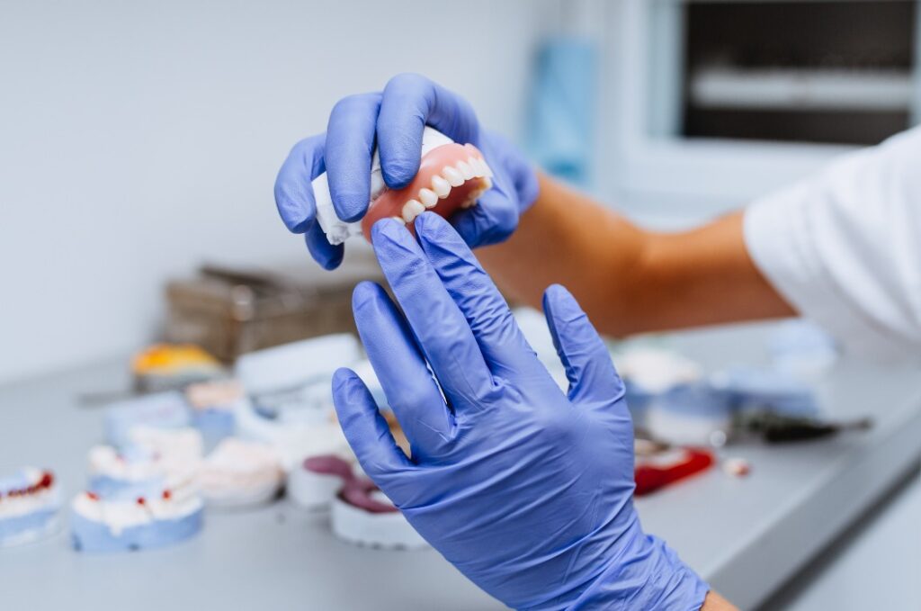 Zahnersatz, prothetische Arbeit. Nahaufnahme der Hände des Prothetikers bei der Arbeit an der Prothese.